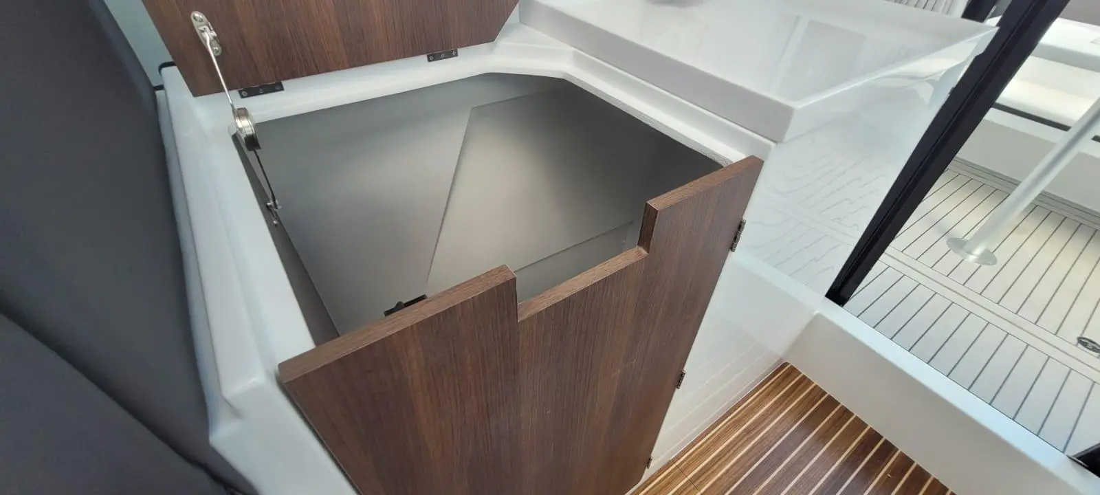 Open storage compartment on a boat, featuring wooden doors, with a white interior and a striped wooden floor visible.
